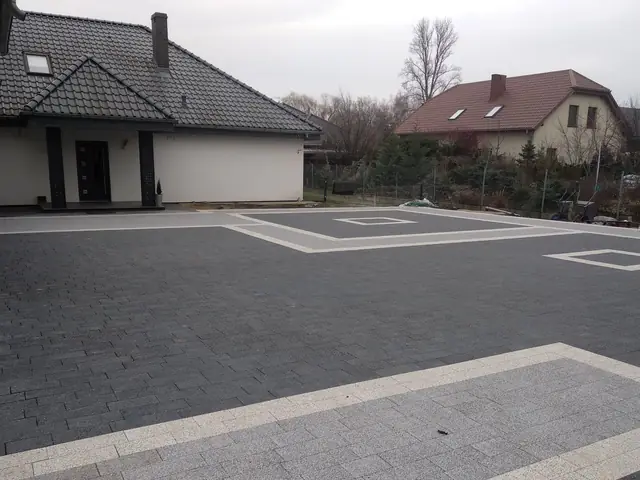 Podjazd z grafitowej kostki brukowej z jasnym obramowaniem i wzorem przed domem